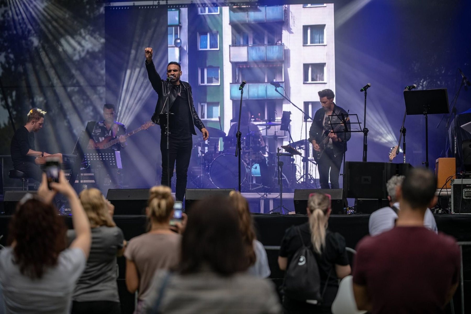 Sami Harb na plenerowej scenie z zespołem na żywo, publiczność nagrywa występ