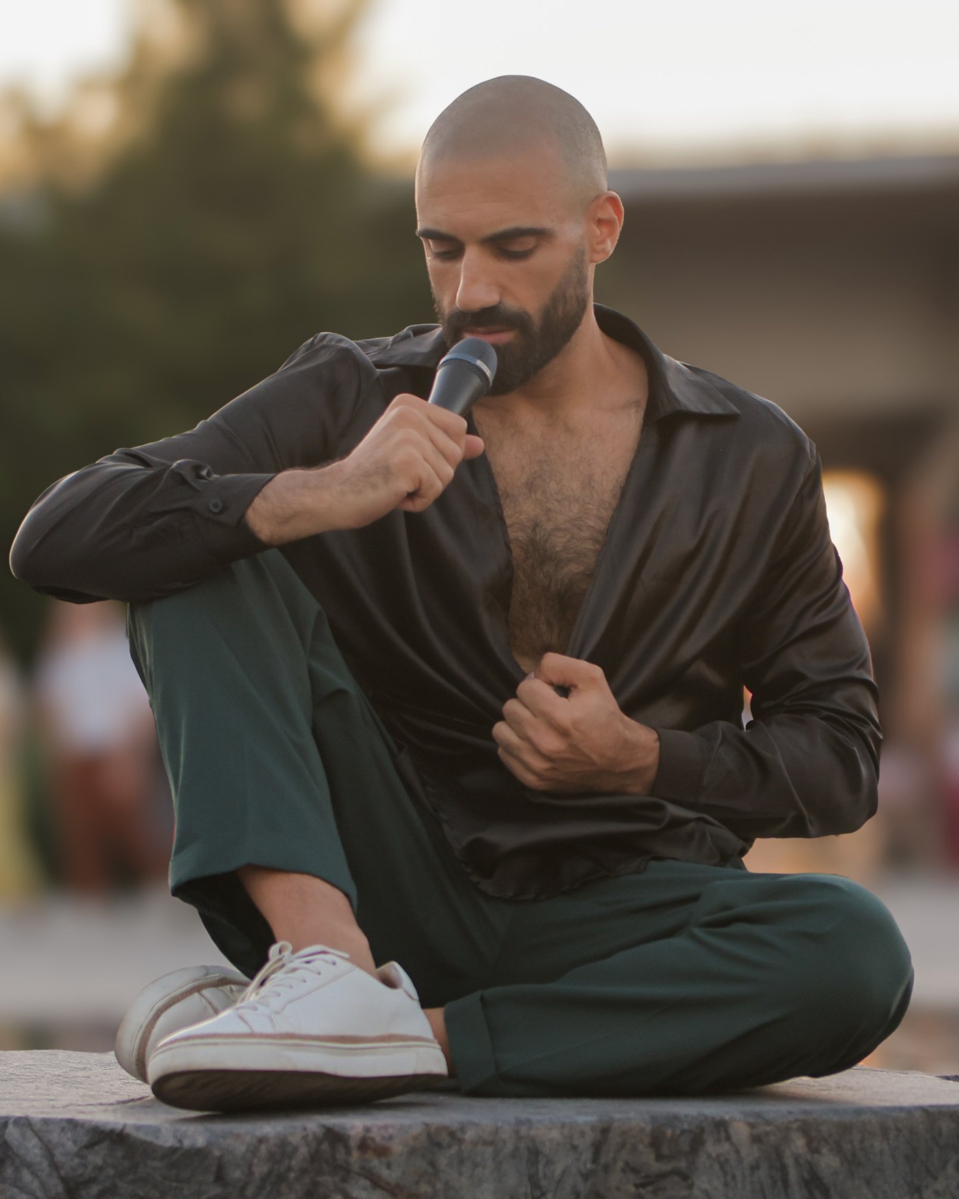 Sami Harb siedzi na zewnątrz w złotym świetle i cicho śpiewa do mikrofonu